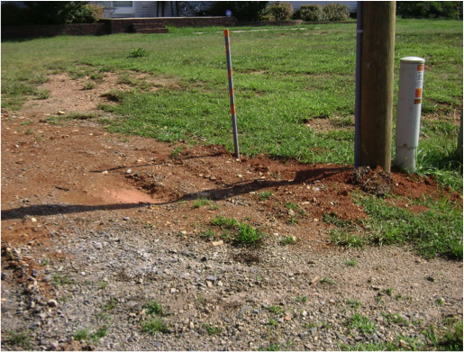 image of outdoor area around electric pole where the dirt has been dug up and paid back in a relatively flat manner, with some tire treads showing, and minimal loss of grass cover