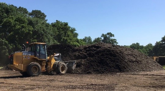 City staff operating earth mover to move large pile of compost