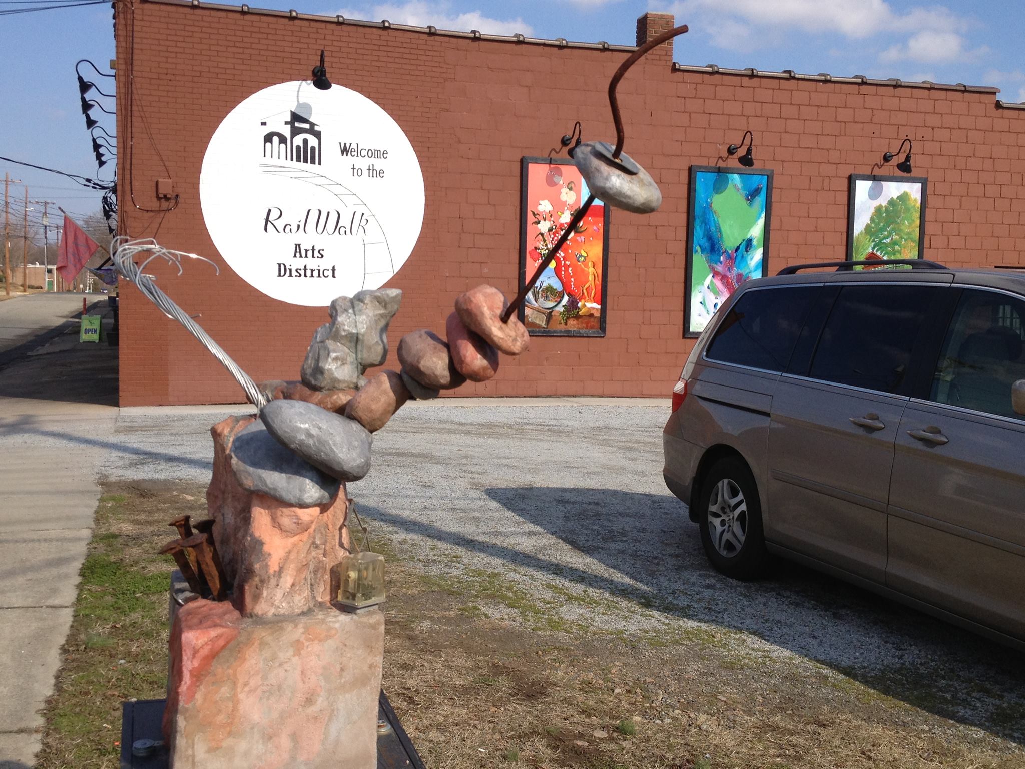 View of the railwalk signage, with an outdoor sculpture posed at the parking lot's corner