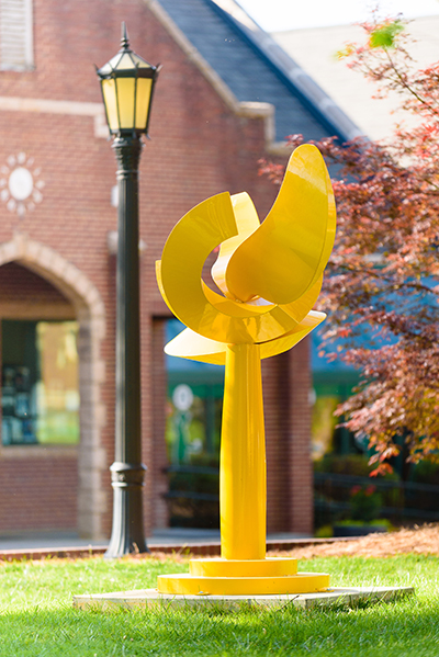 a large outdoor sculpture painted bright yellow, placed in front of a local college